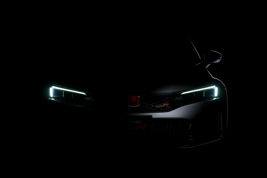 暗闇の中から、ホンダ・シビックタイプRのシャープなLEDヘッドライトと、中央に輝く赤いHマーク、そしてグリルに刻まれた「TYPE R」のエンブレムだけが浮かび上がっている、ミステリアスで迫力のあるフロントビューのティーザー写真。